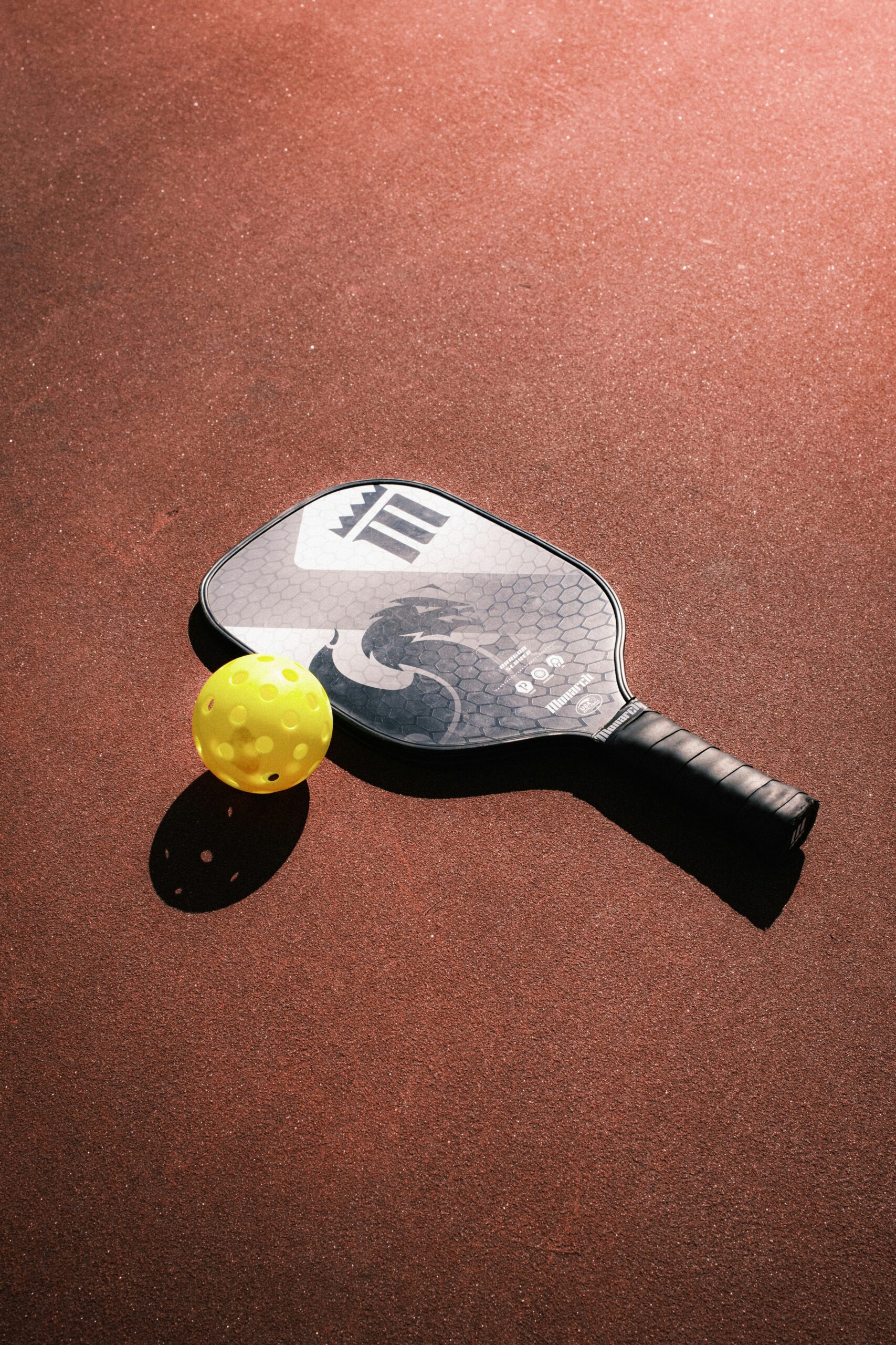 Pickleball paddle and yellow ball on outdoor court surface in Northbrook Illinois - sports acupuncture helps prevent tennis elbow and knee pain for pickleball players